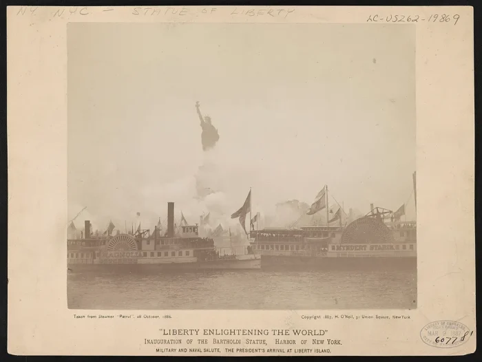Sepia-toned photograph of steamboats gathered in New York Harbor during the dedication of the Statue of Liberty on October 28, 1886, with the statue faintly visible through heavy fog in the background.